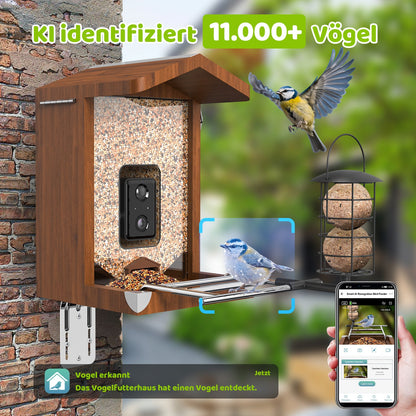 Holz‑Vogelhaus mit integrierter Kamera an Backsteinwand, Futterschacht mit Körnern, Blaumeise auf Metallstange, Smartphone zeigt App mit Vogel‑Erkennung und Schriftzug ‚KI identifiziert 11.000+ Vögel‘